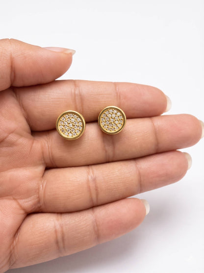 Gold stud earrings held between fingers on a white background