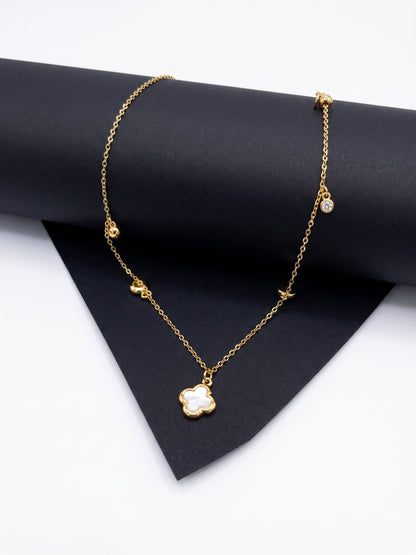 Gold necklace with a clover-shaped pendant on a black surface