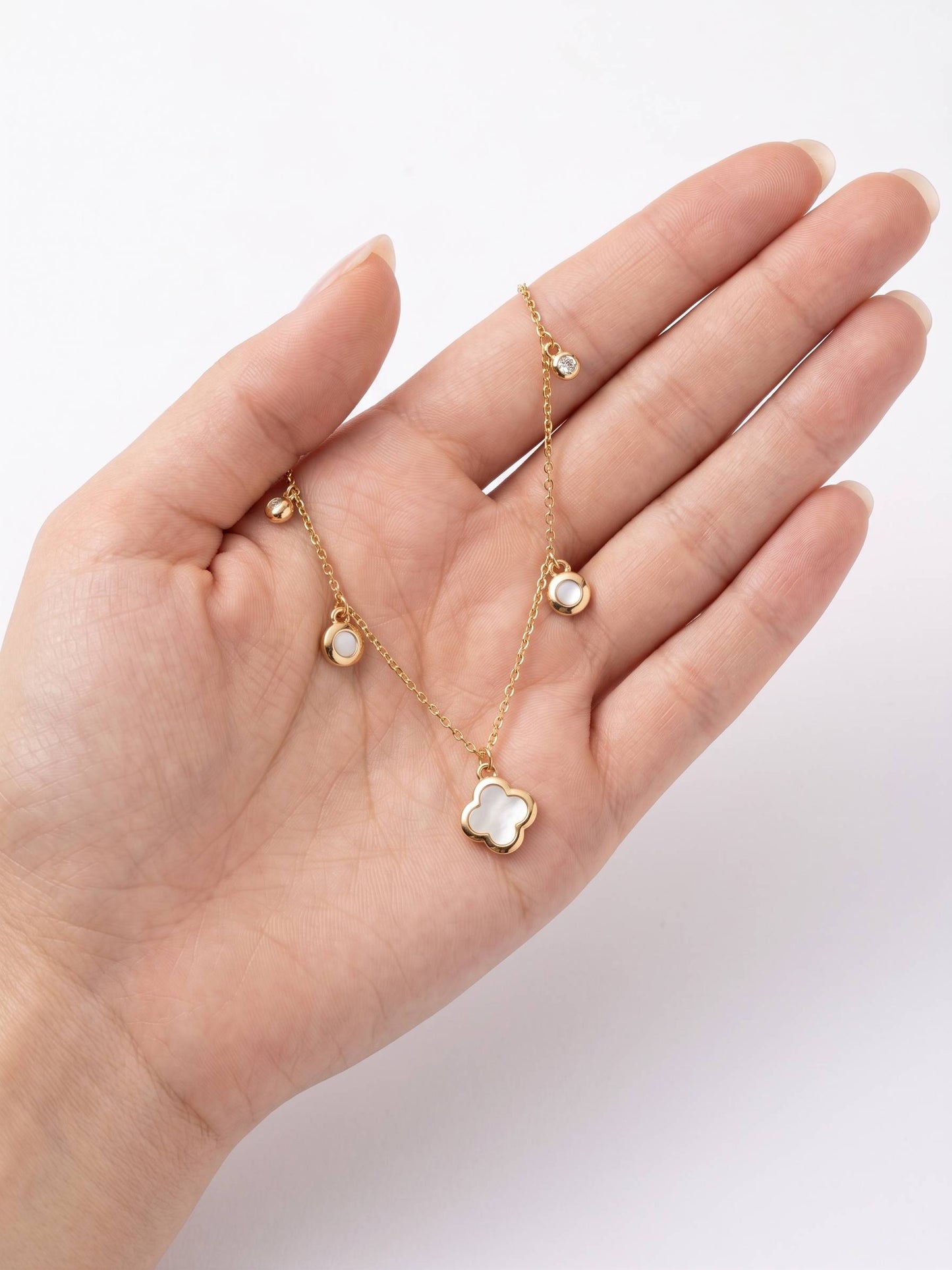 Hand holding a delicate gold necklace with floral pendant on a white background