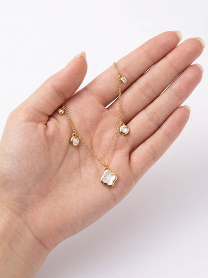 Hand holding a delicate gold necklace with floral pendant on a white background