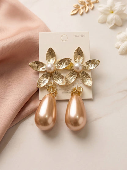 Gold floral earrings with pearl accents on a card, held by a hand with a soft background.