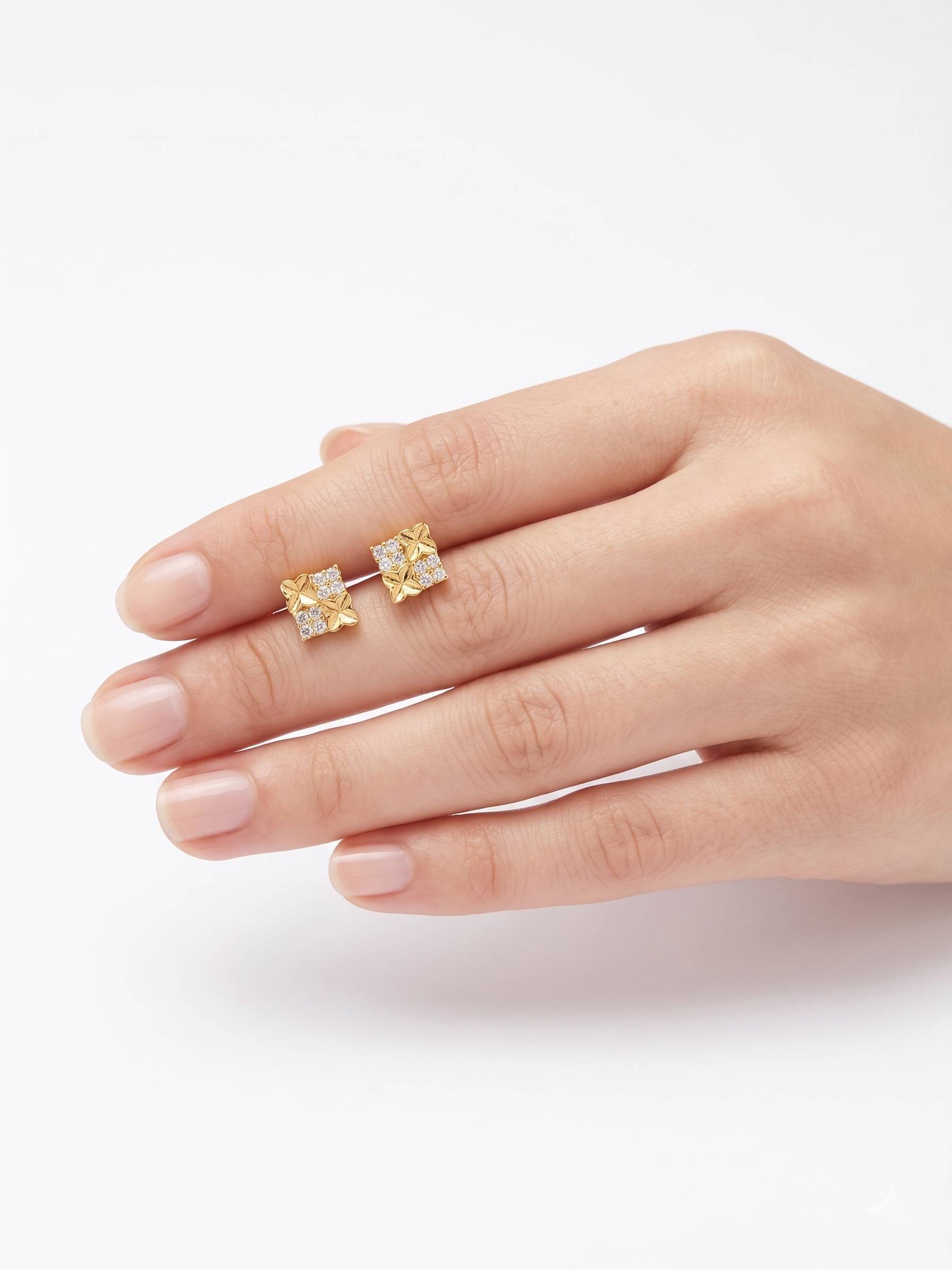 Gold earrings with clear stones held by a hand on a white background