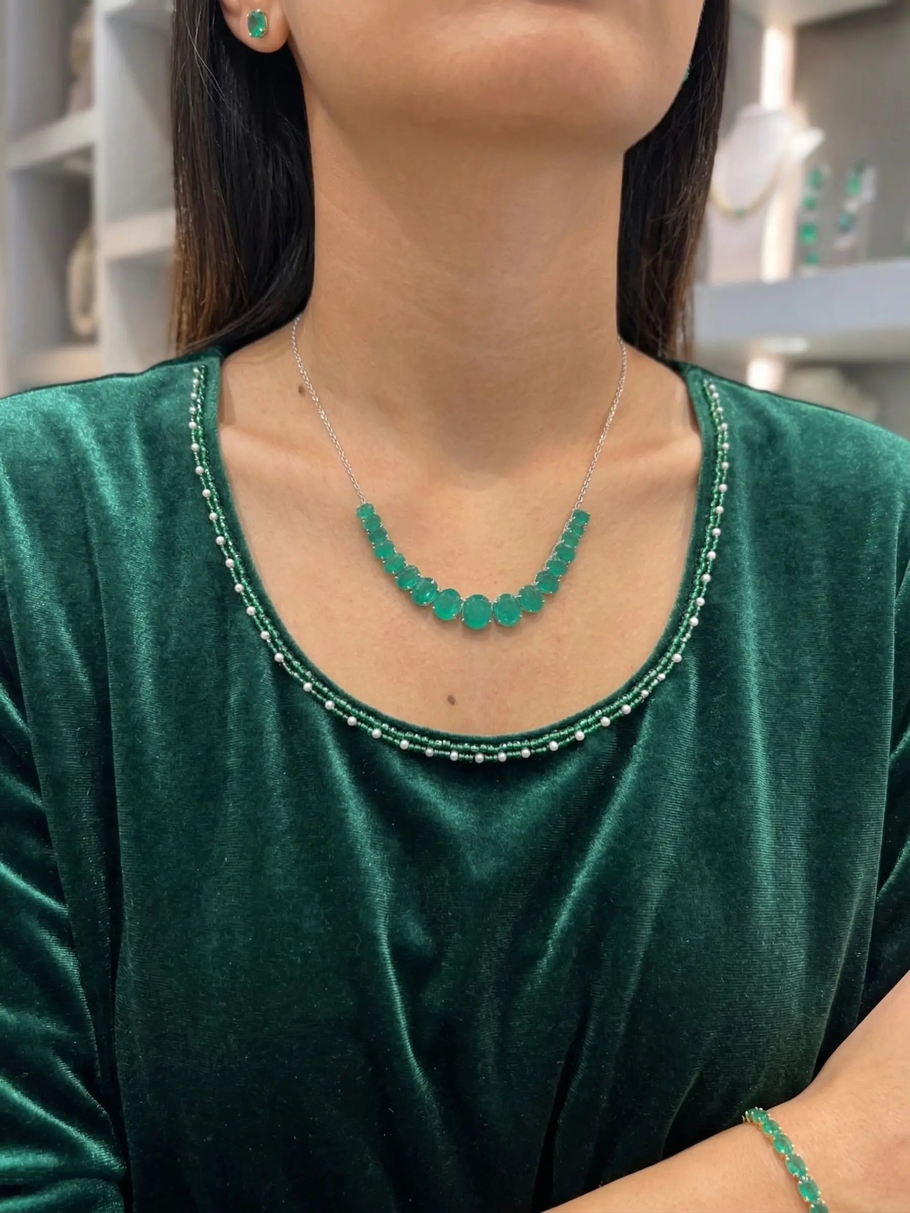 Person wearing a green necklace and earrings against a blurred indoor background