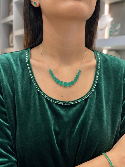 Person wearing a green necklace and earrings against a blurred indoor background