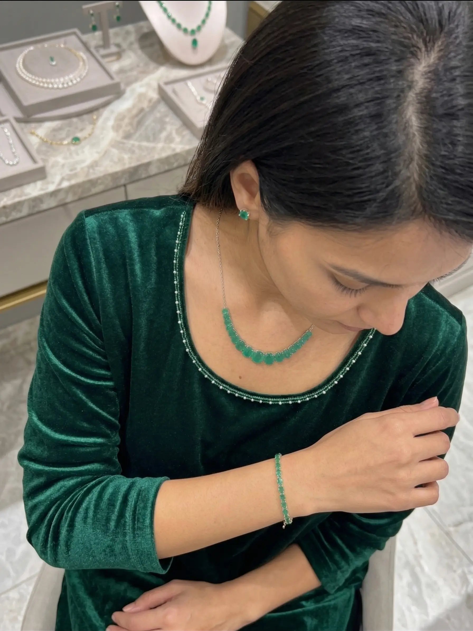 Woman wearing a green velvet top with matching jewelry in a jewelry store setting.