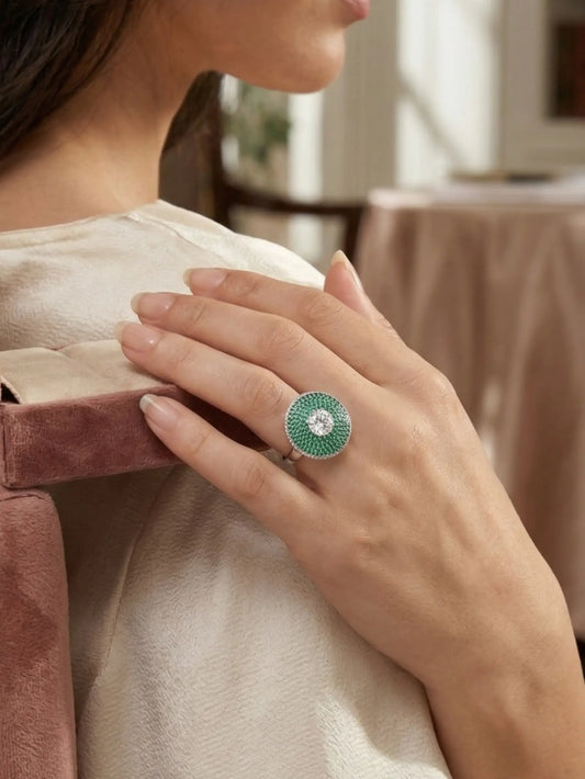 Close-up of a hand wearing a green ring with a diamond, holding a pink velvet box.