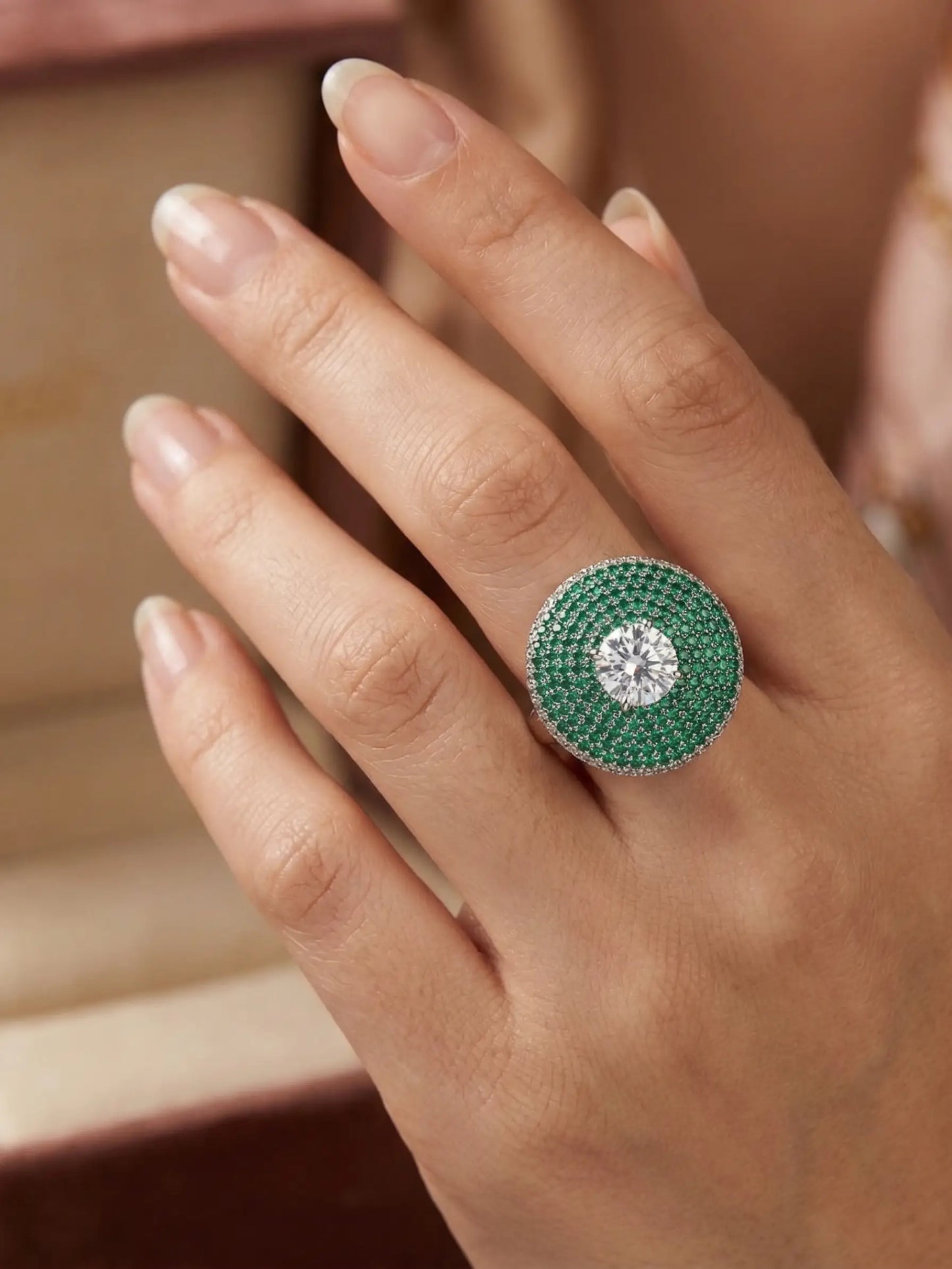 Close-up of a hand wearing a green ring with a diamond on a neutral background