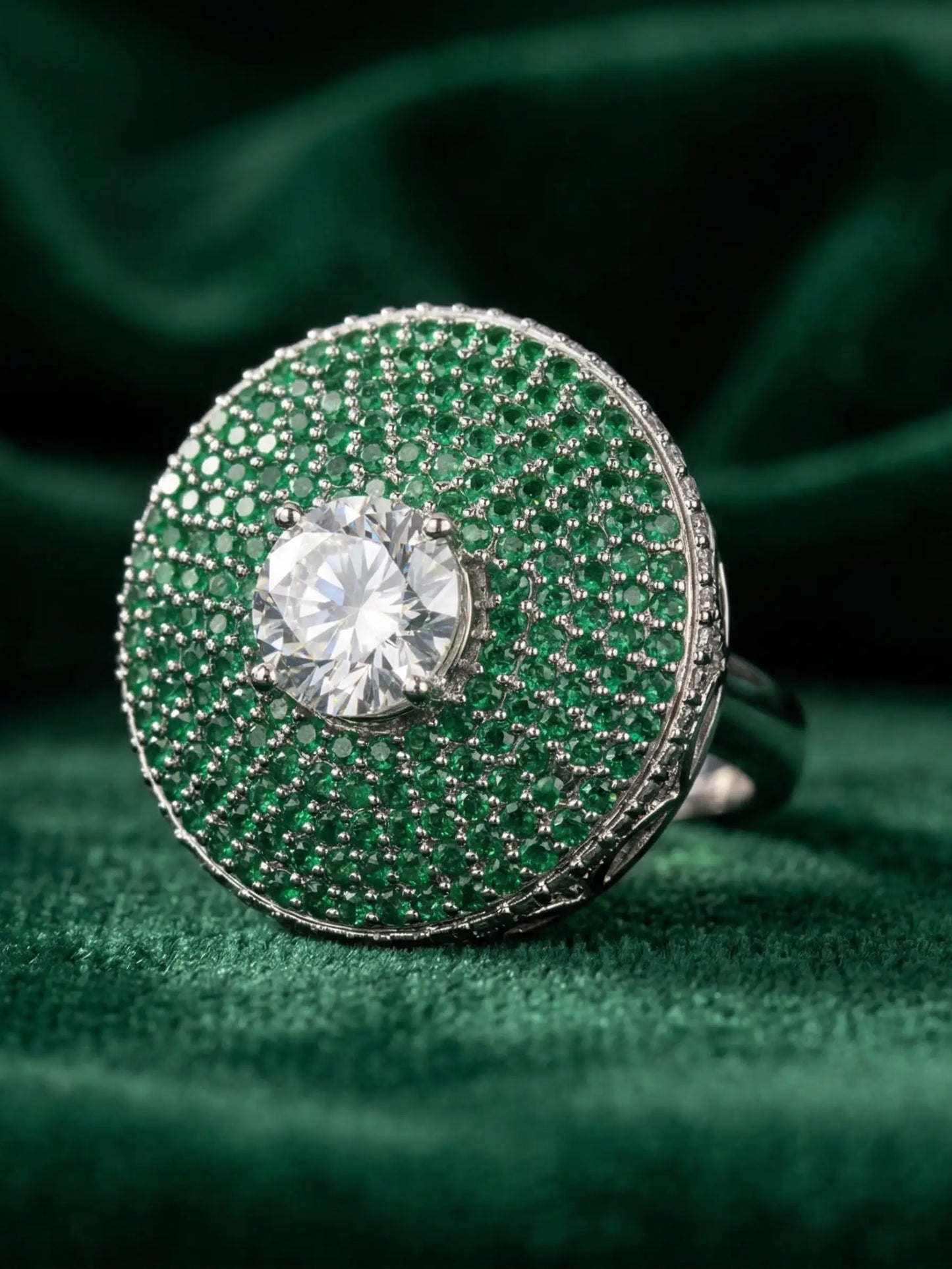 Green gemstone ring with a central diamond on a green fabric background