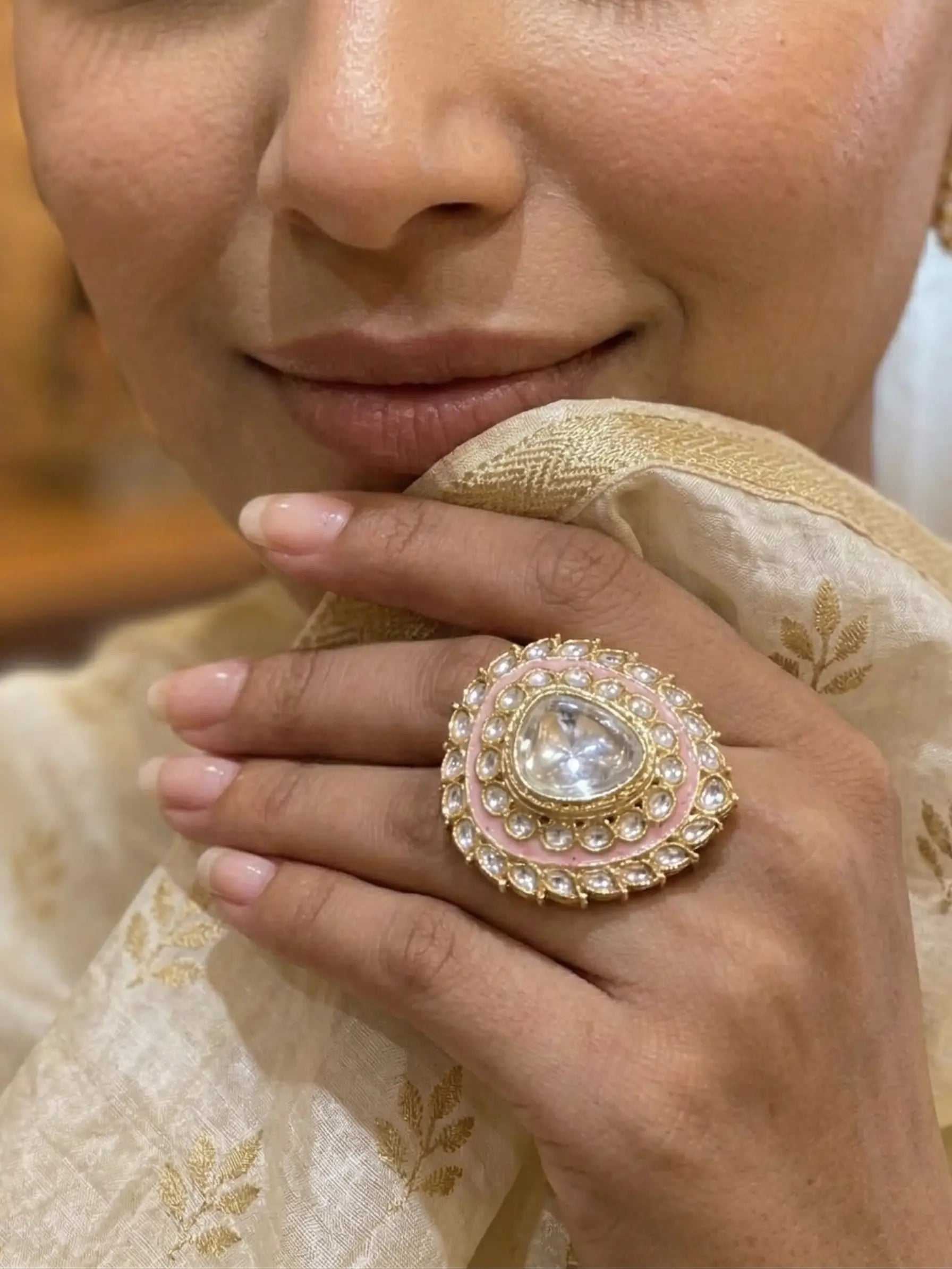 Close-up of a hand wearing an ornate ring with a pearl-like center, set against a blurred background.