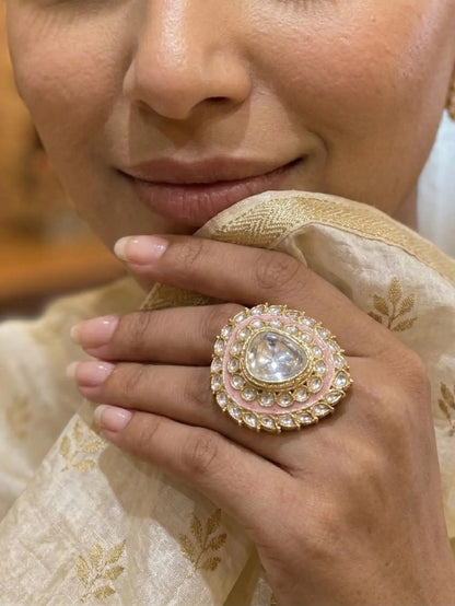 Close-up of a hand wearing an ornate ring with a pearl-like center, set against a blurred background.