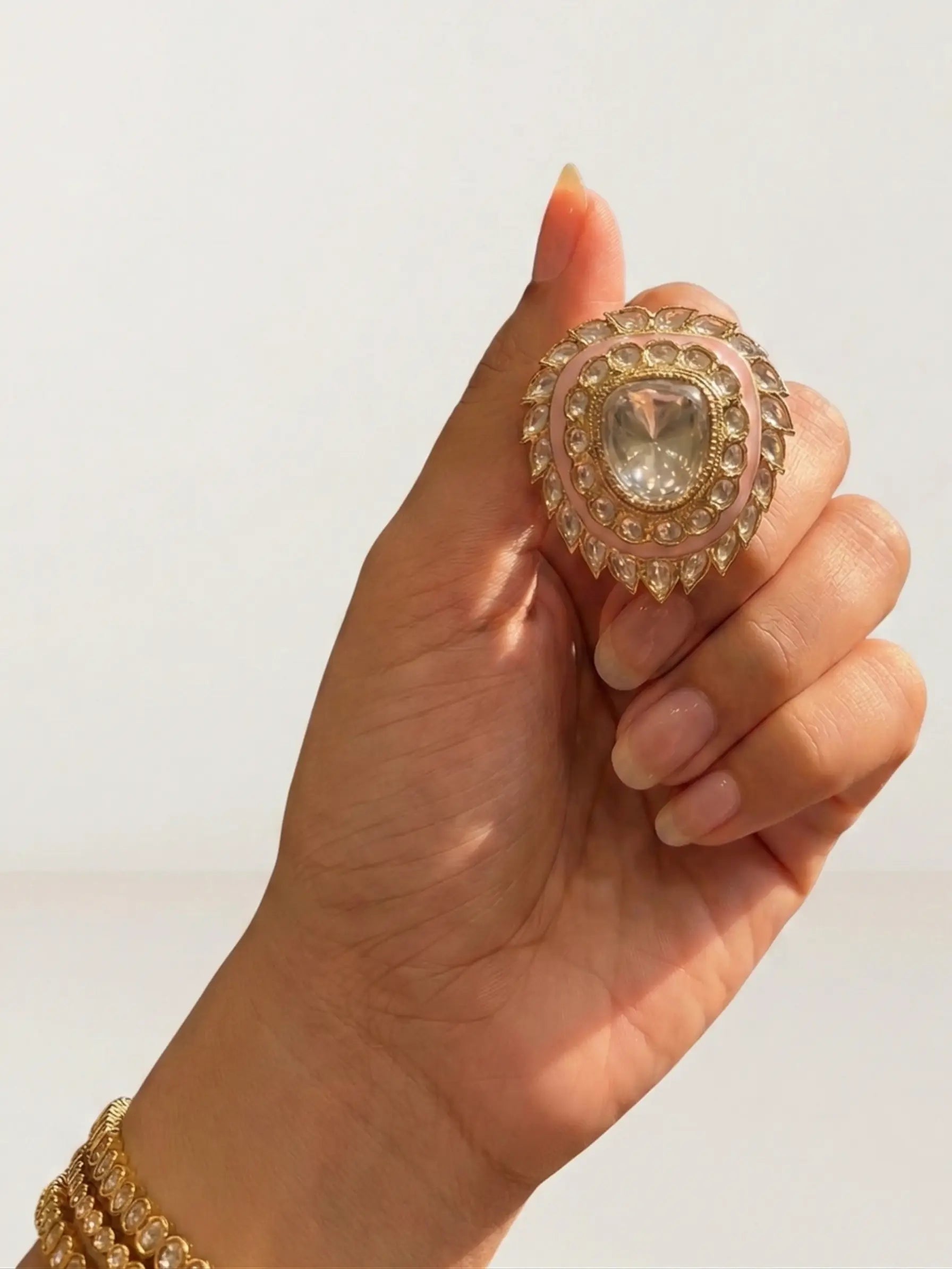 Hand holding a decorative ring with a clear gemstone against a neutral background