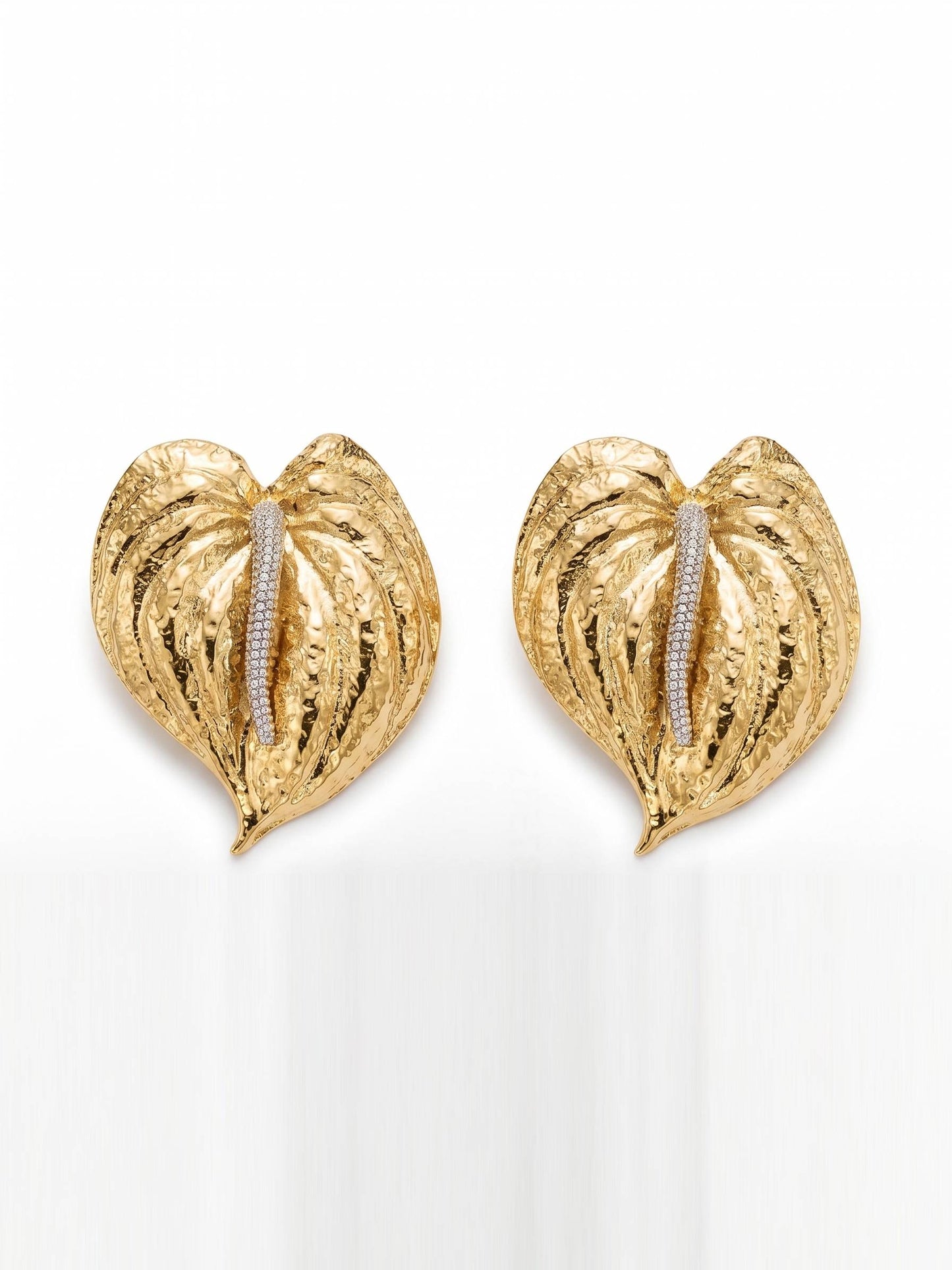 Gold leaf-shaped earrings with embedded stones on a white background