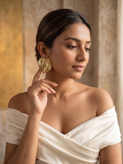 Woman wearing gold earrings and a white off-shoulder top against a warm-toned curtain background