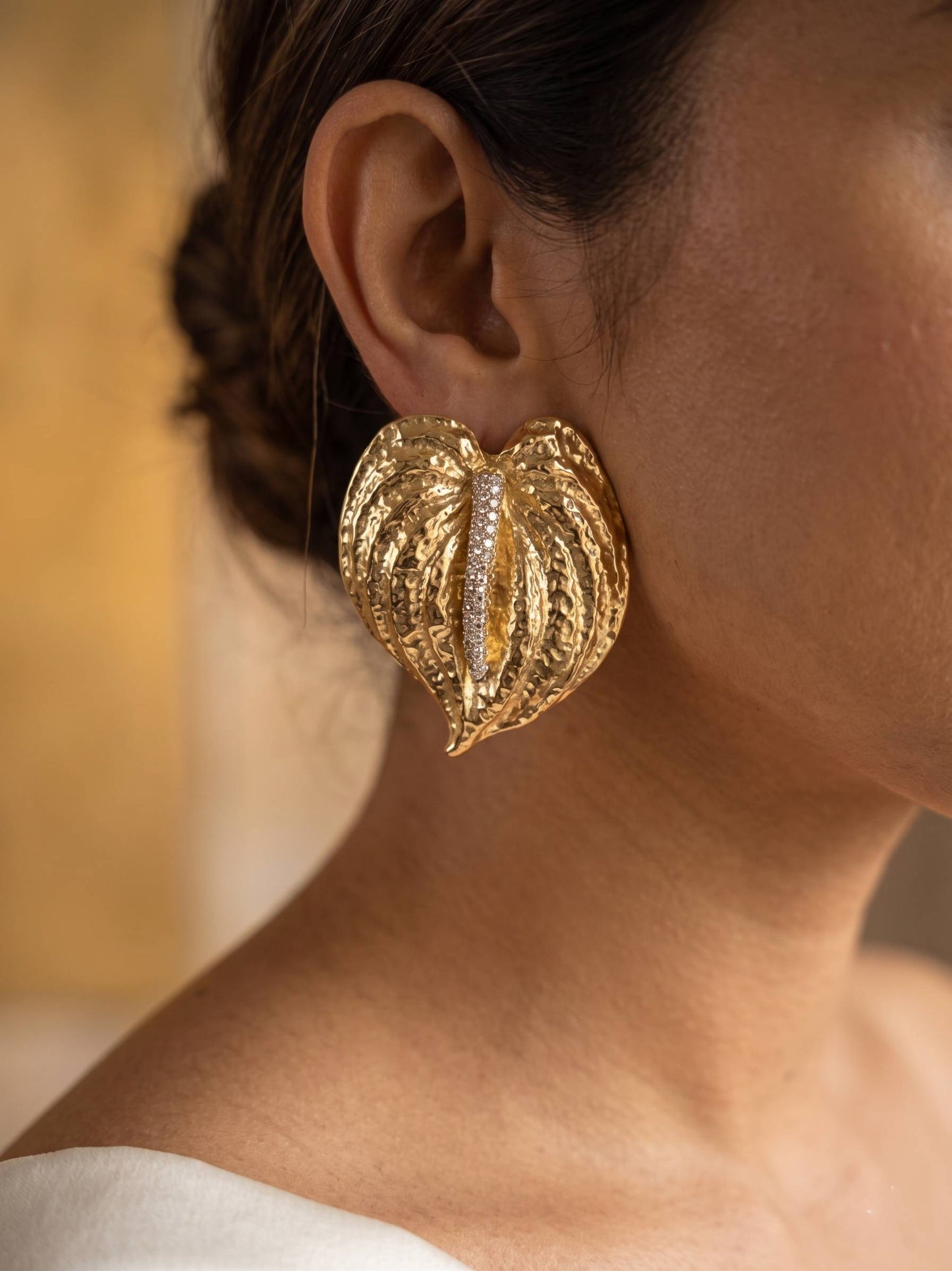 Gold leaf-shaped earring worn by a person with a blurred background