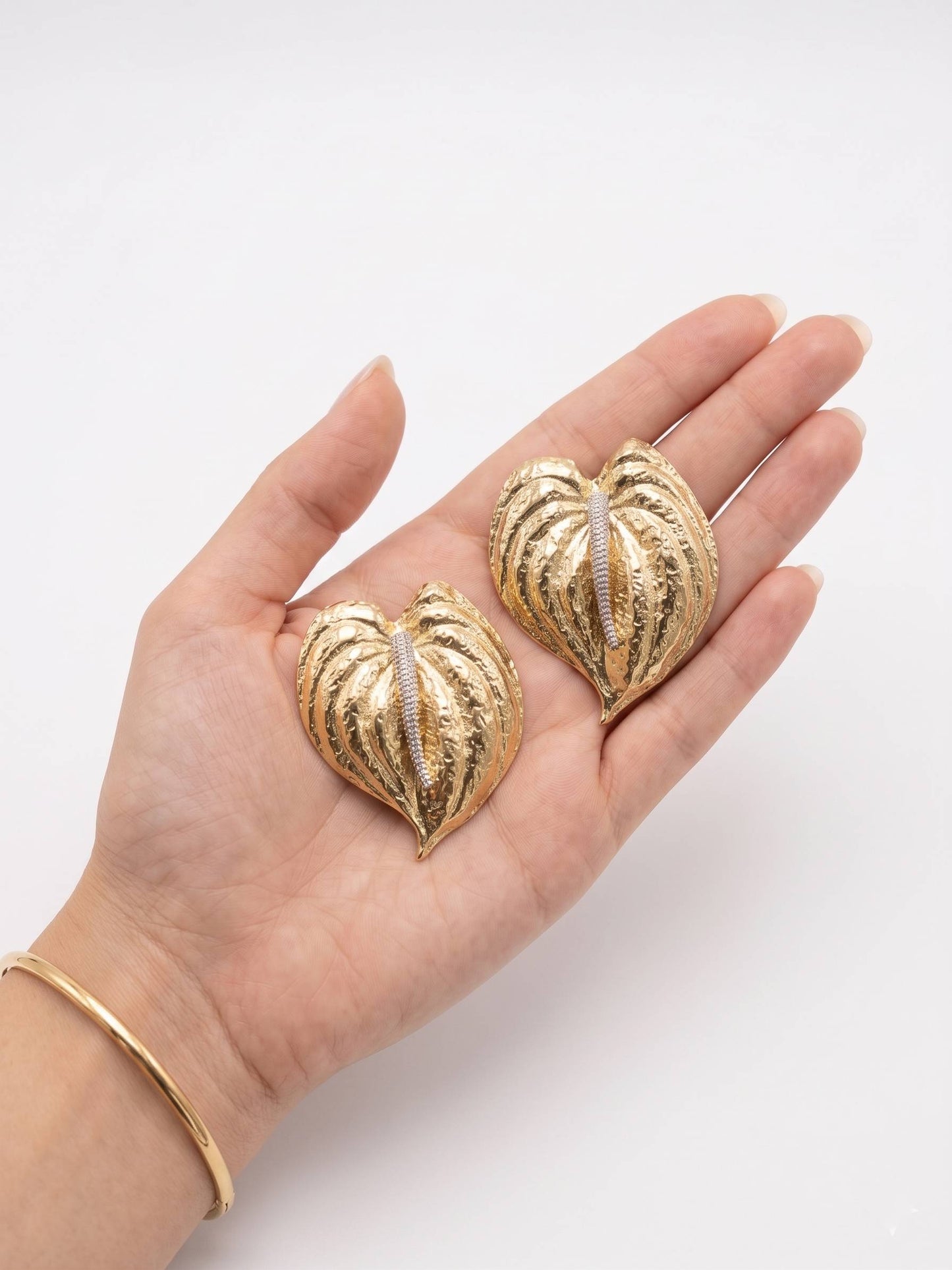 Gold heart-shaped earrings held in a hand on a white background