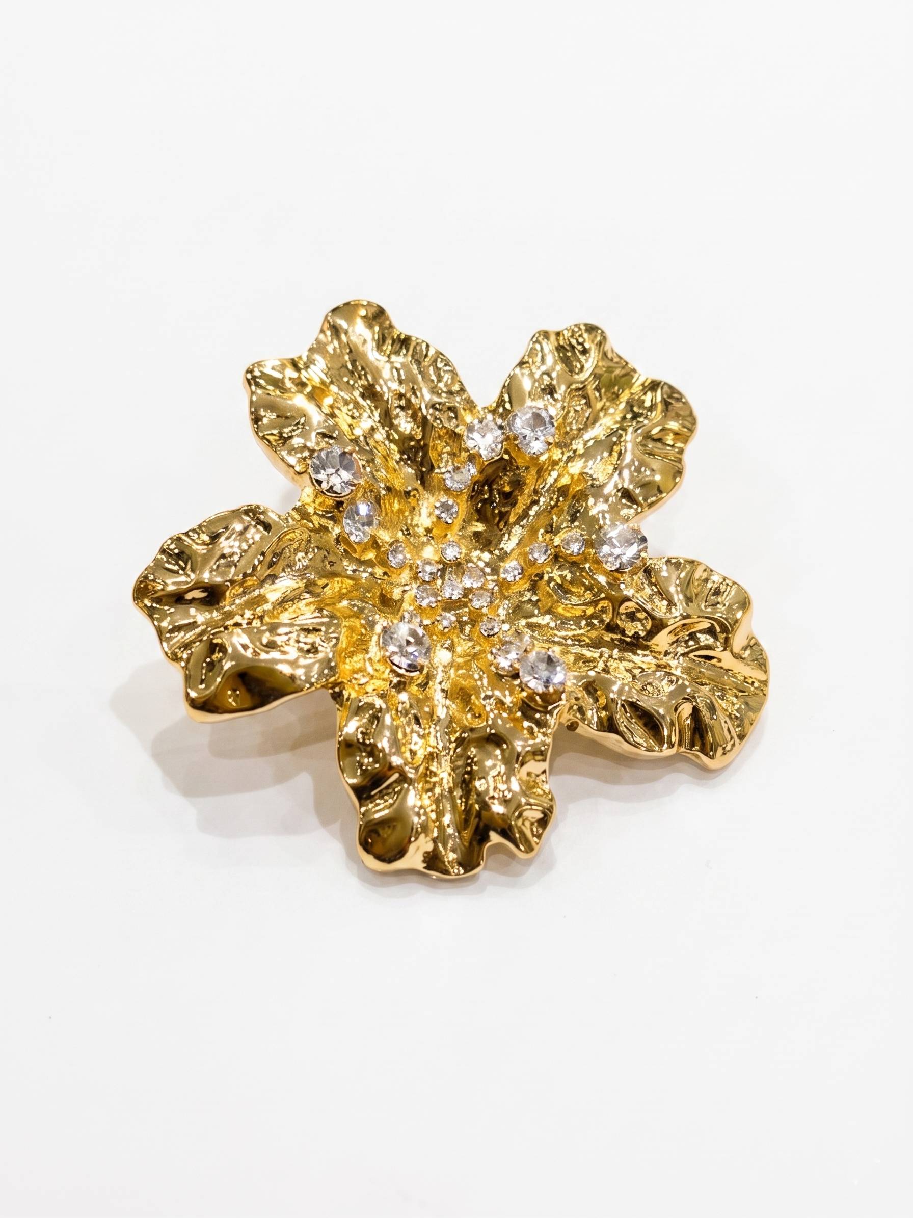 Gold flower-shaped earring with embedded crystals on a white background