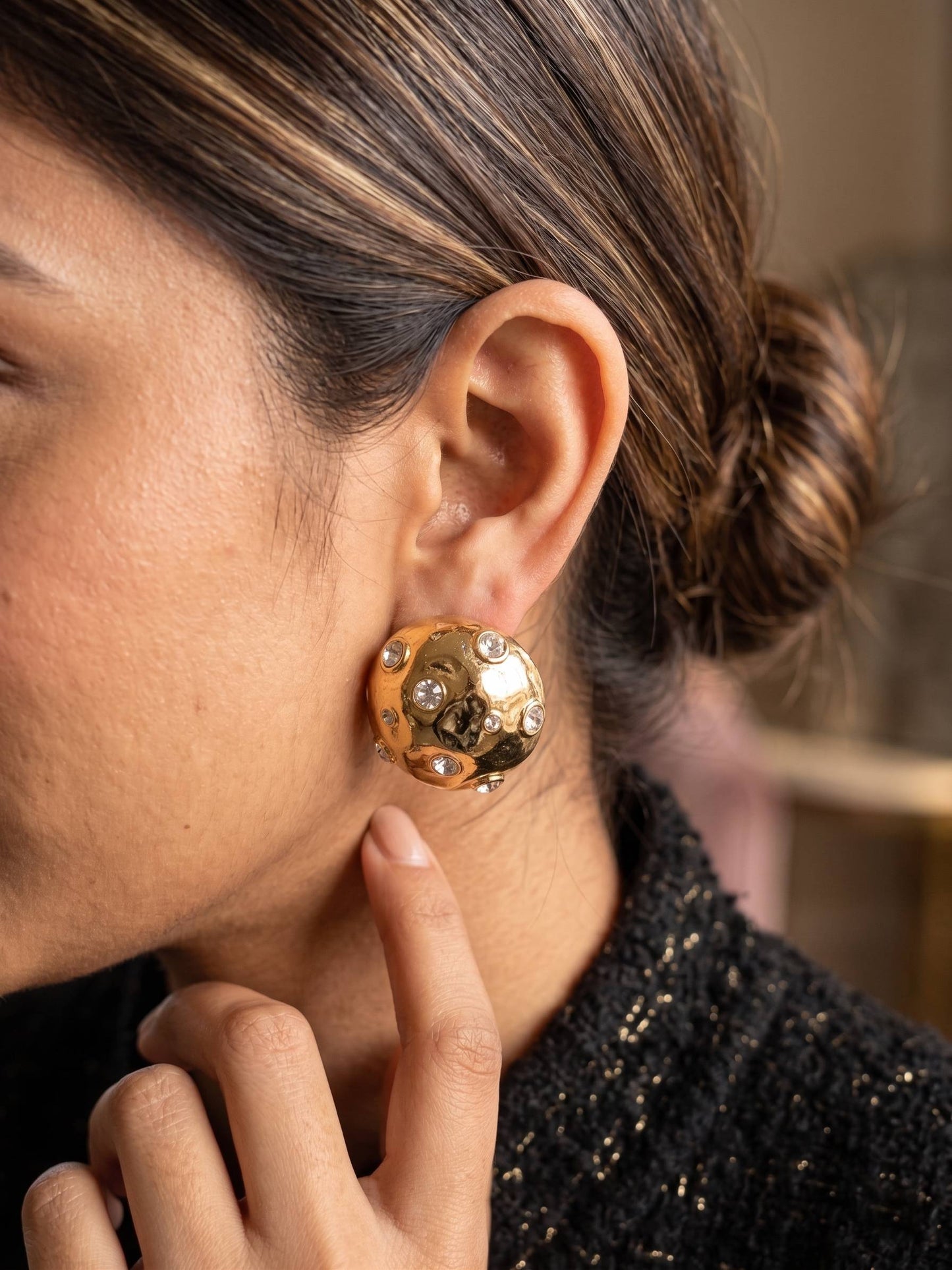 Close-up of a person wearing a gold earring with a blurred background