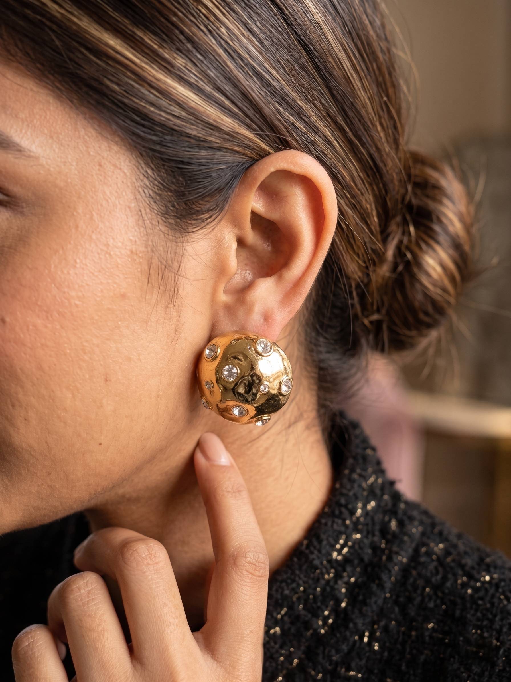 Close-up of a person wearing a gold earring with a blurred background