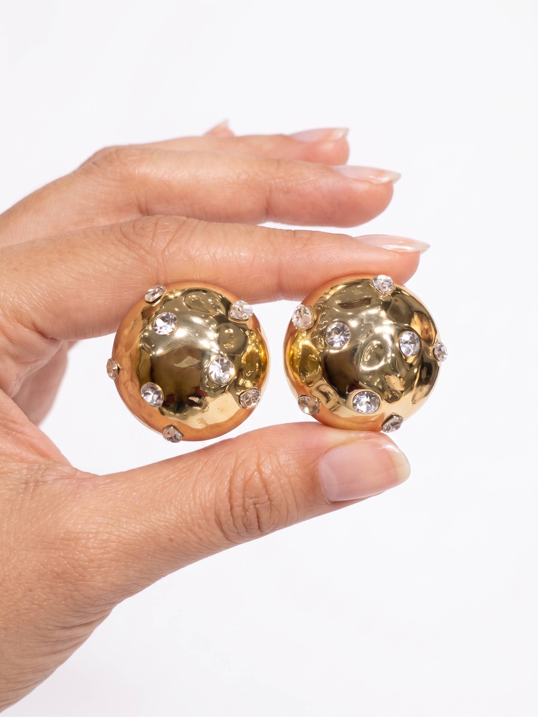 Gold earrings with gemstones held by a hand on a white background