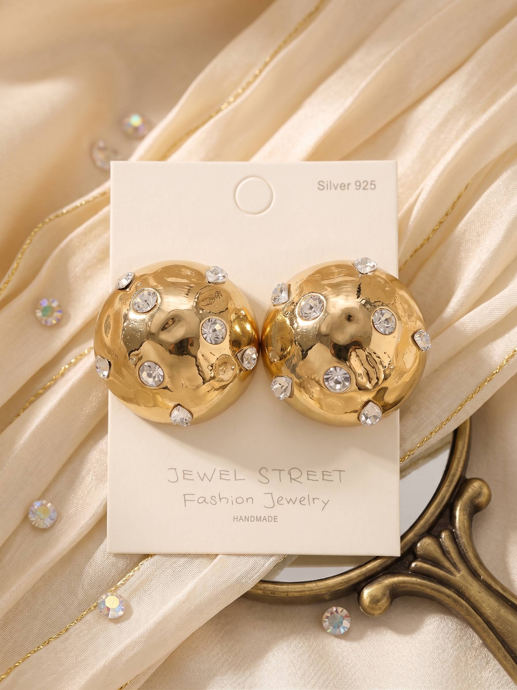 Gold earrings with gemstones on a 'Jewel Street' branded card against a beige fabric background.
