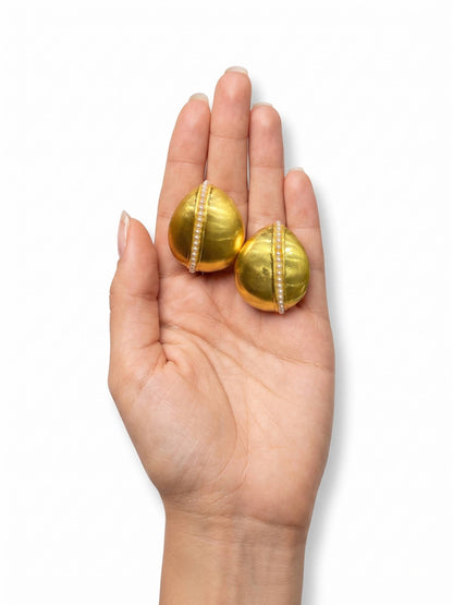 Gold earrings held in a hand on a white background
