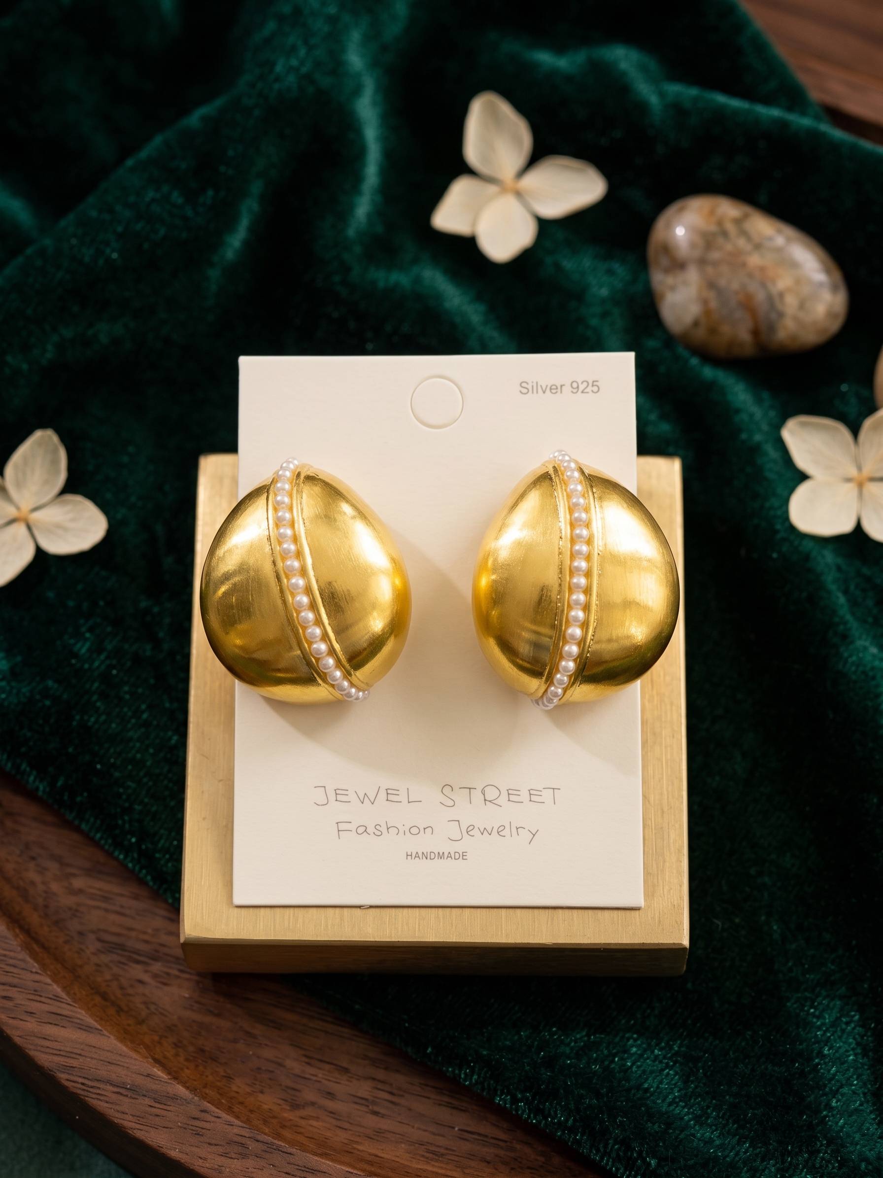 Gold earrings on a Jewel Street card with a green fabric background