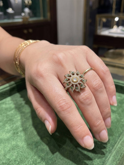 Hand wearing a decorative ring on a green surface with blurred jewelry store background