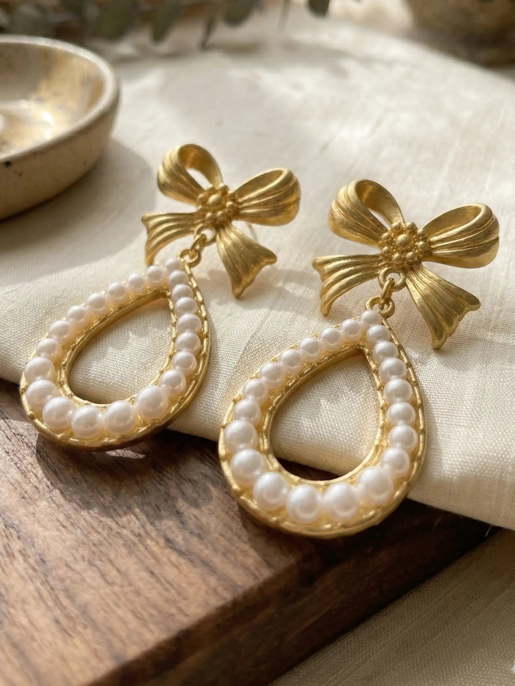 Elegant gold-finish bow earrings with teardrop pearl dangle design