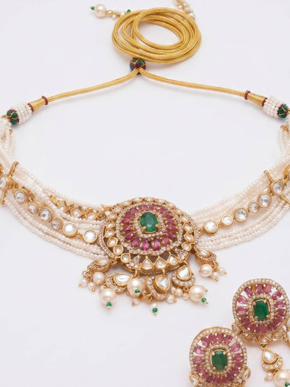 An ornate traditional Indian jewelry set featuring a multi-strand necklace with a central gold and green stone medallion, matching drop earrings, and a gold chain strap, displayed on a clean white background.