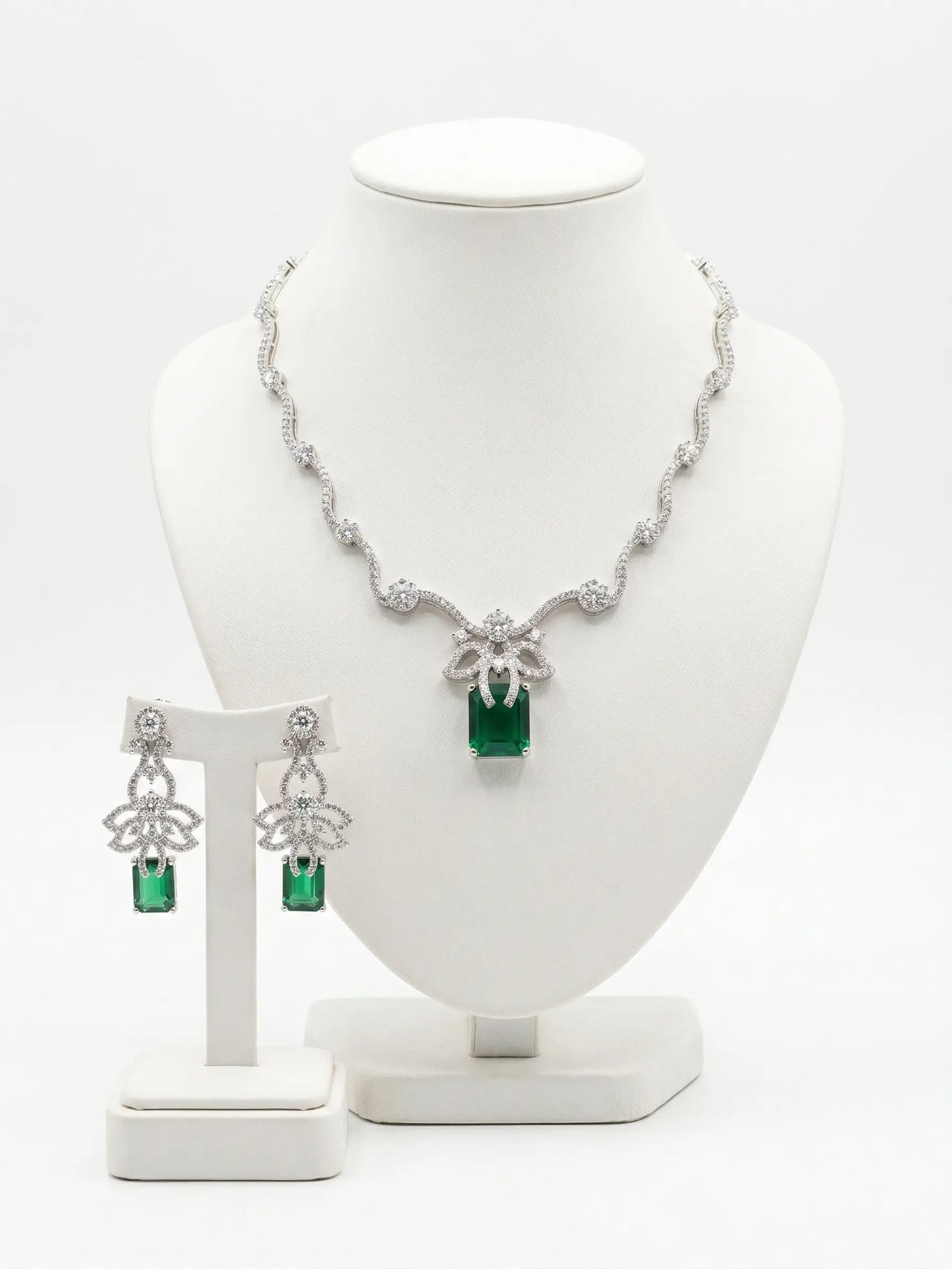 Jewelry set with necklace and earrings featuring green gemstones on a white stand.