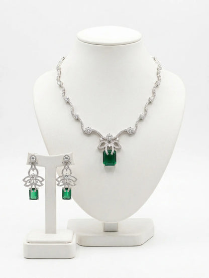 Jewelry set with necklace and earrings featuring green gemstones on a white stand.