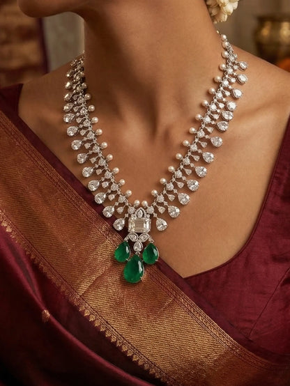 Elegant diamond necklace with emerald pendants on a person wearing a maroon saree.
