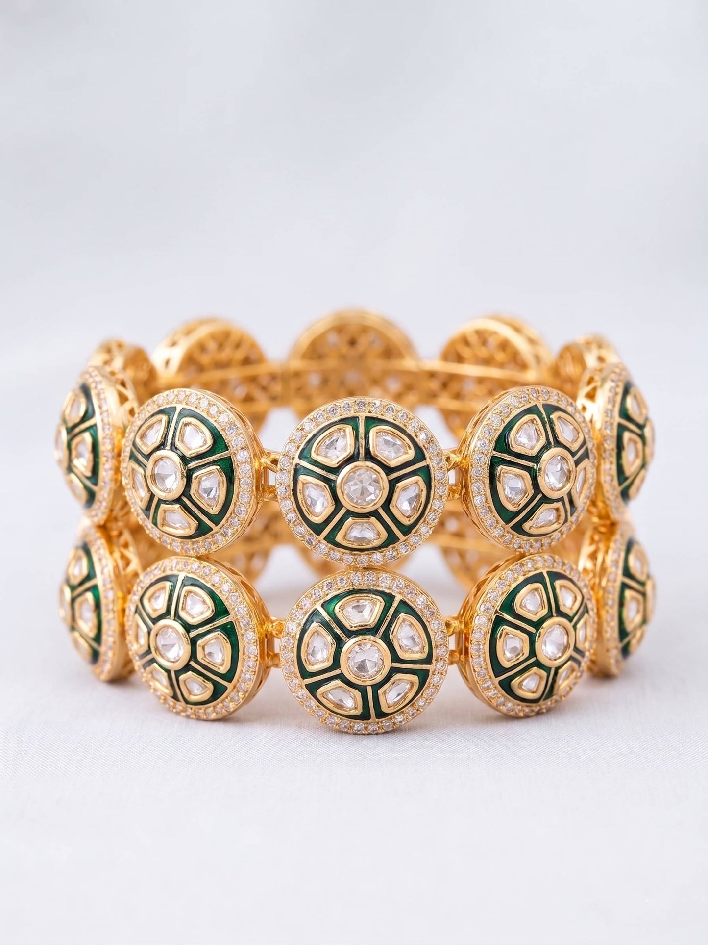 Gold bracelet with green and white circular patterns on a light gray background