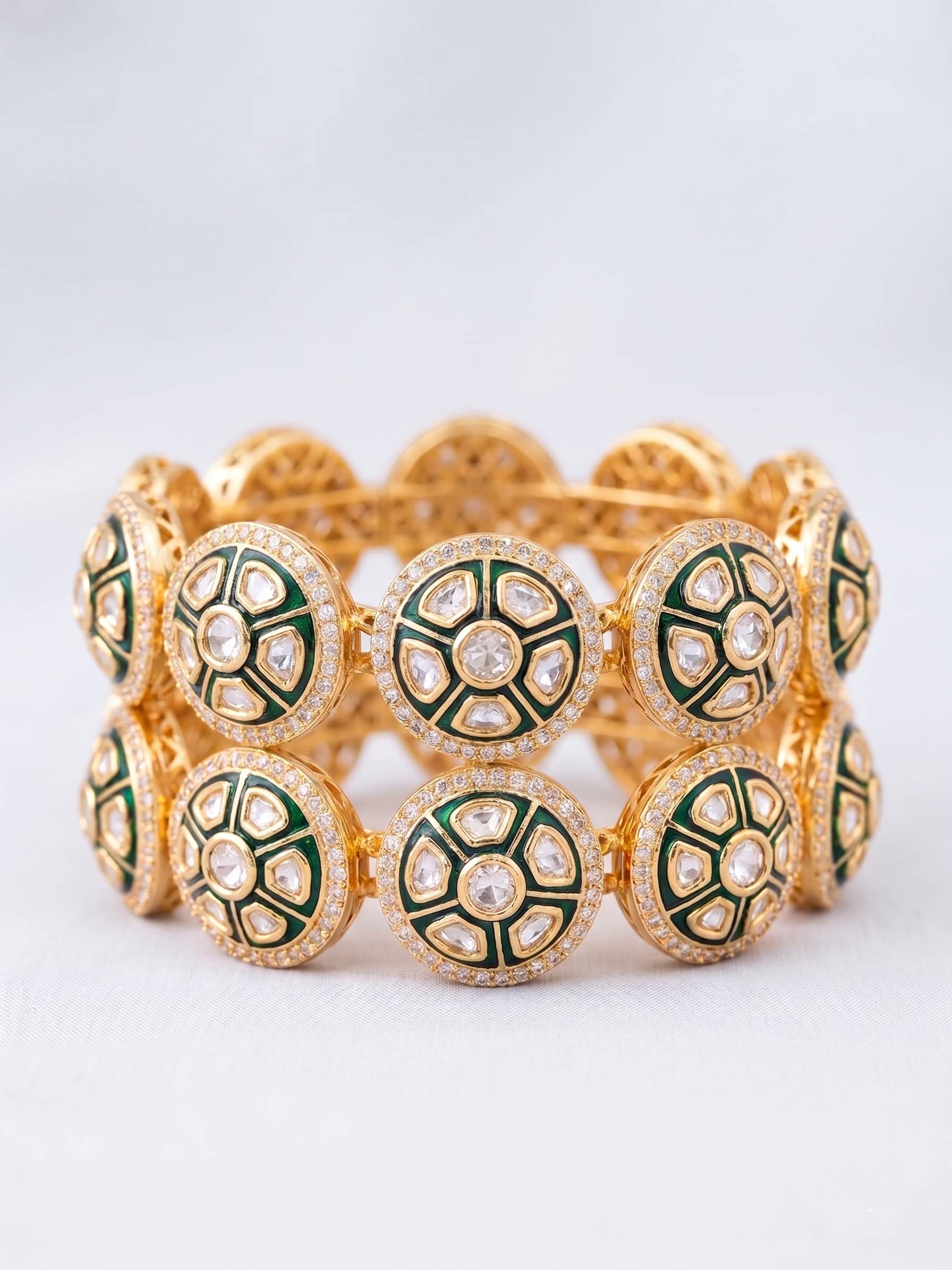 Gold bracelet with green and white circular patterns on a light gray background