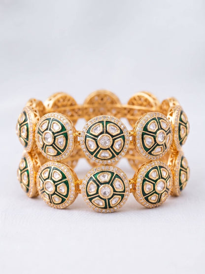 Gold bracelet with green and white circular patterns on a light gray background