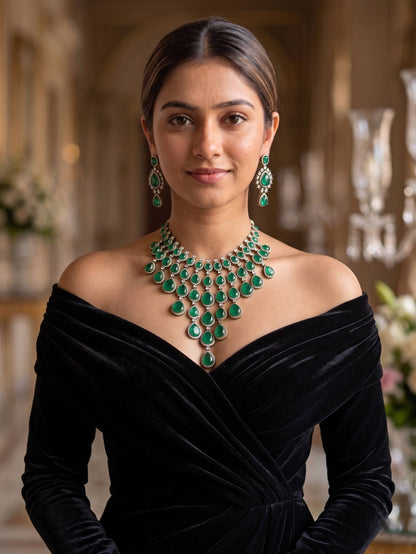 Woman wearing a black off-shoulder dress with emerald green jewelry in an elegant indoor setting.