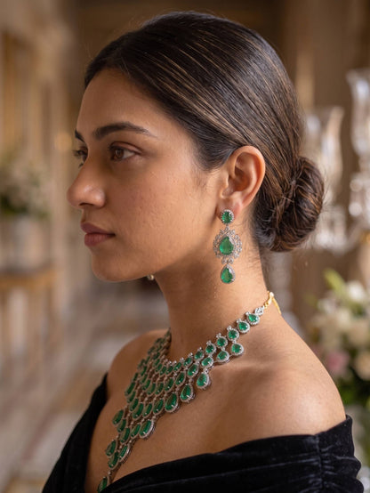 Woman wearing emerald jewelry set with necklace and earrings in a blurred indoor setting