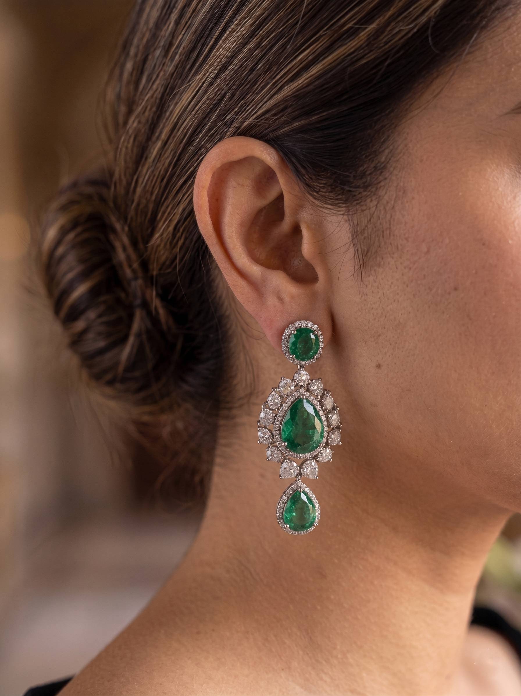 Close-up of a person wearing emerald and diamond earrings with a blurred background