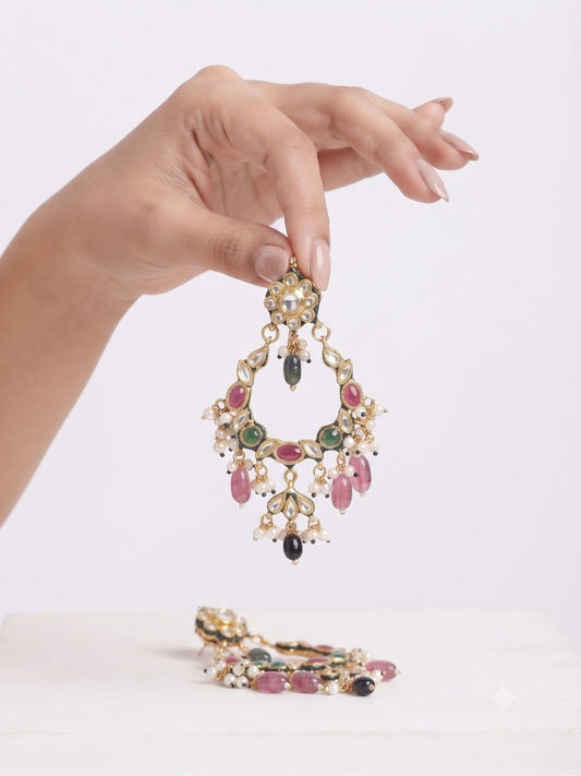A hand holds up a gold-toned traditional Indian choker necklace with colorful stone embellishments, with the matching necklace resting on a white surface below.