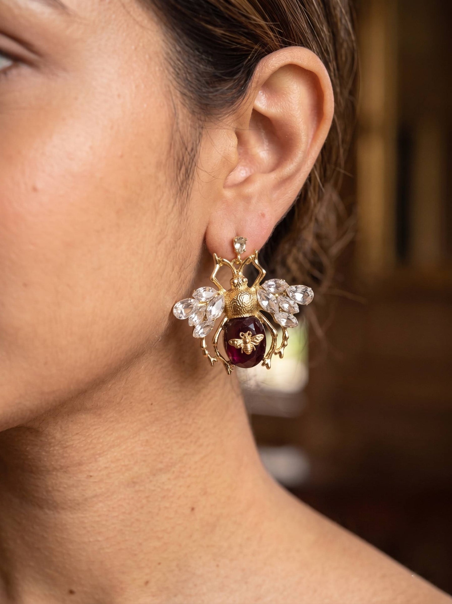 Close-up of a person wearing an ornate gold earring with a red gemstone.