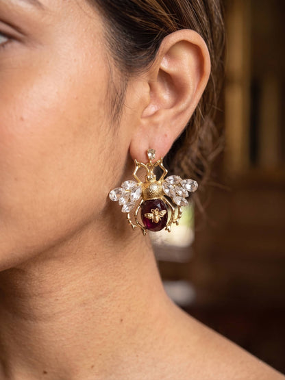 Close-up of a person wearing an ornate gold earring with a red gemstone.