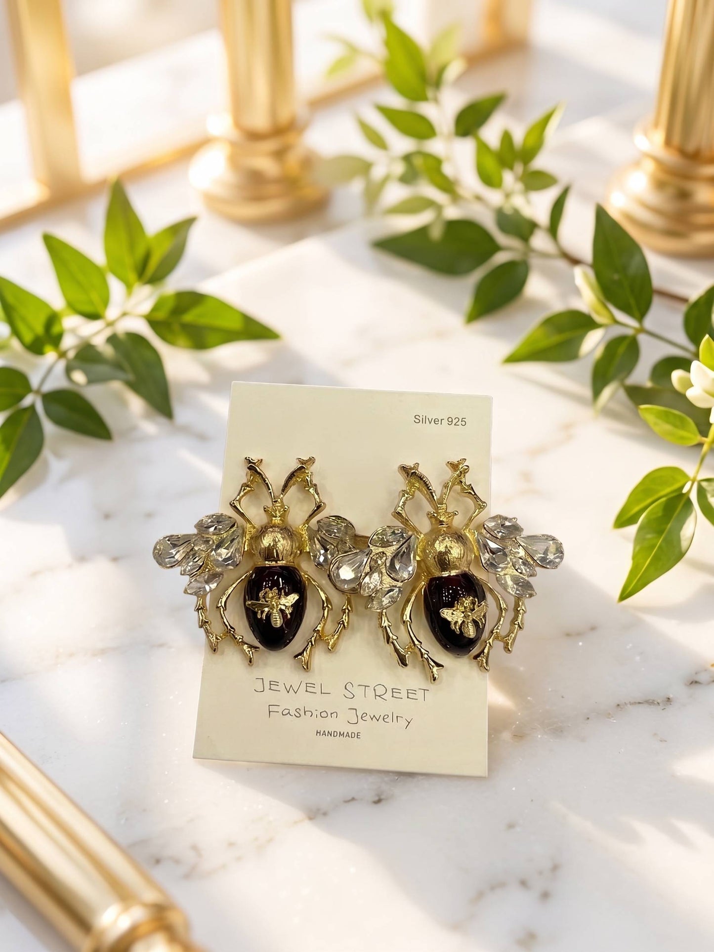 Gold and black earrings on a 'Jewel Street' card with green leaves in the background
