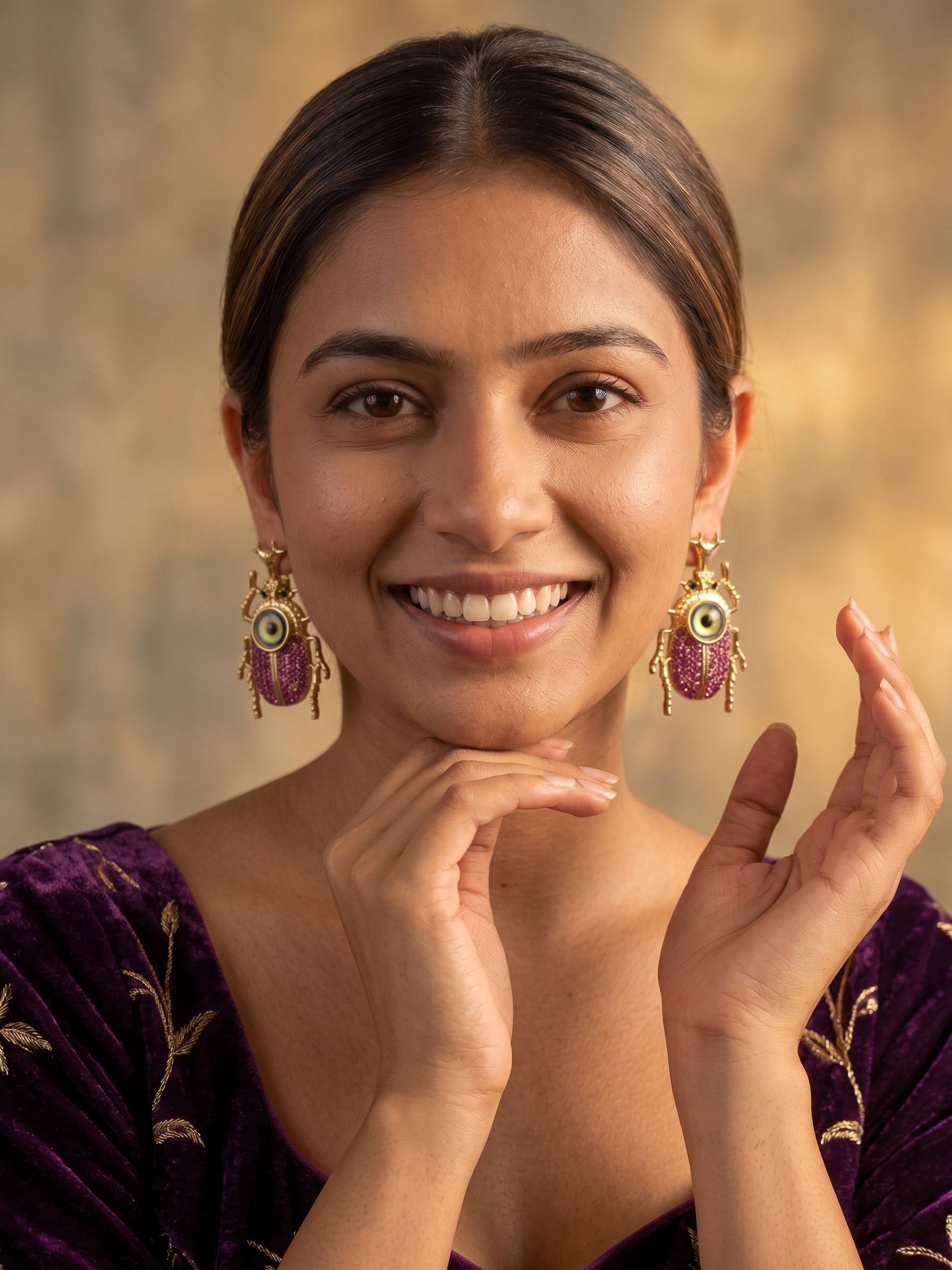 Woman wearing gold earrings with pink gemstones against a warm-toned background