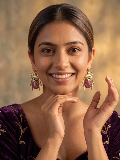 Woman wearing gold earrings with pink gemstones against a warm-toned background