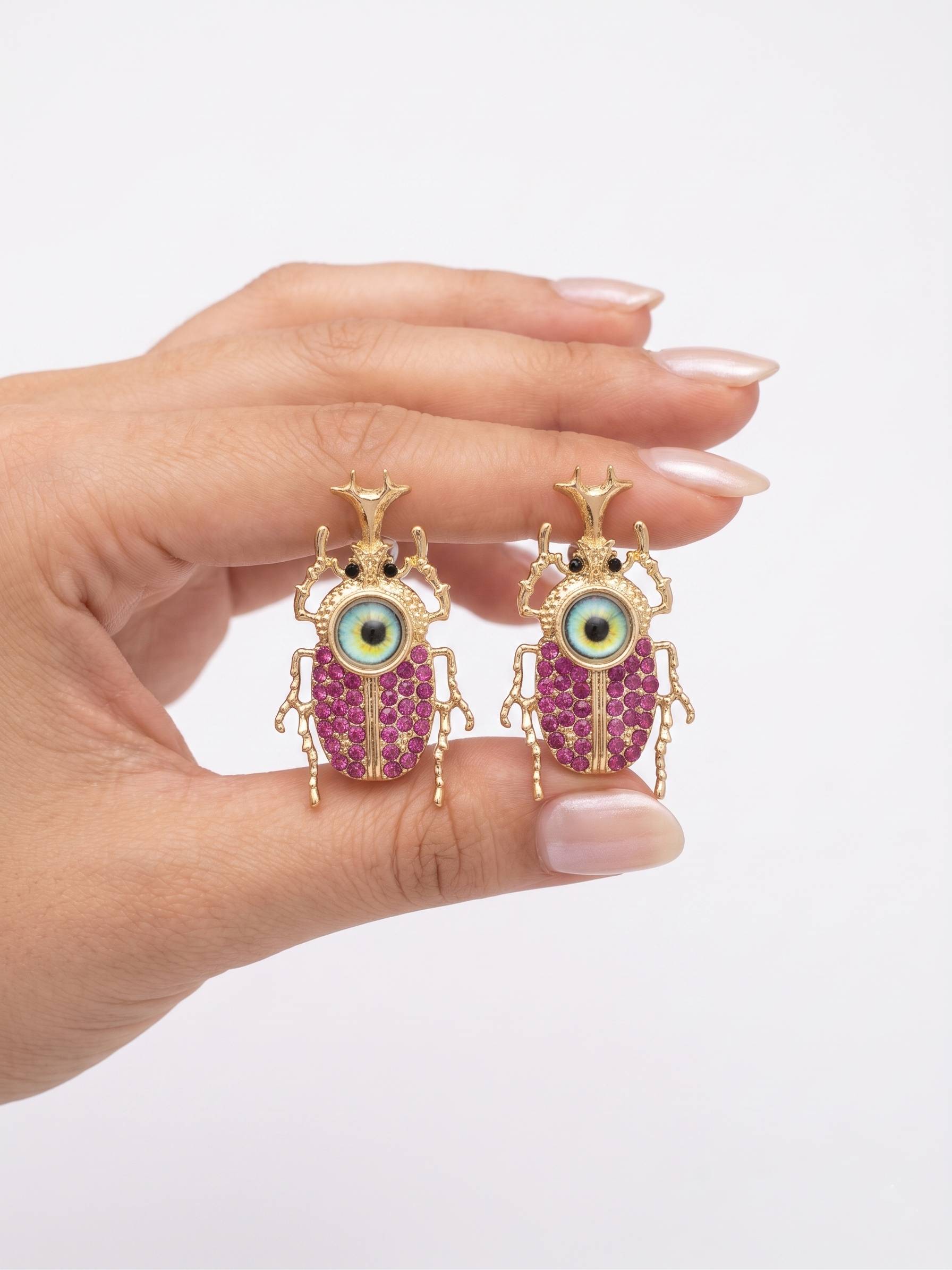 Hand holding a pair of unique earrings with pink gemstones and gold accents on a white background