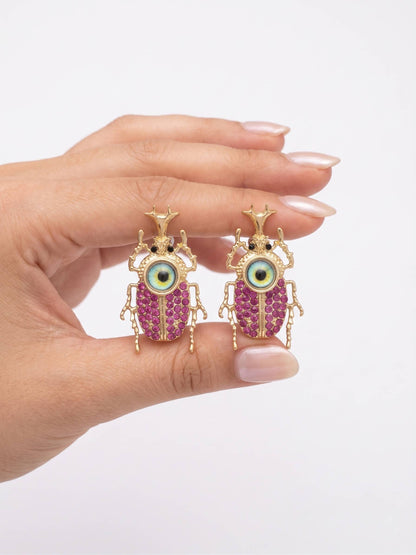 Hand holding a pair of unique earrings with pink gemstones and gold accents on a white background