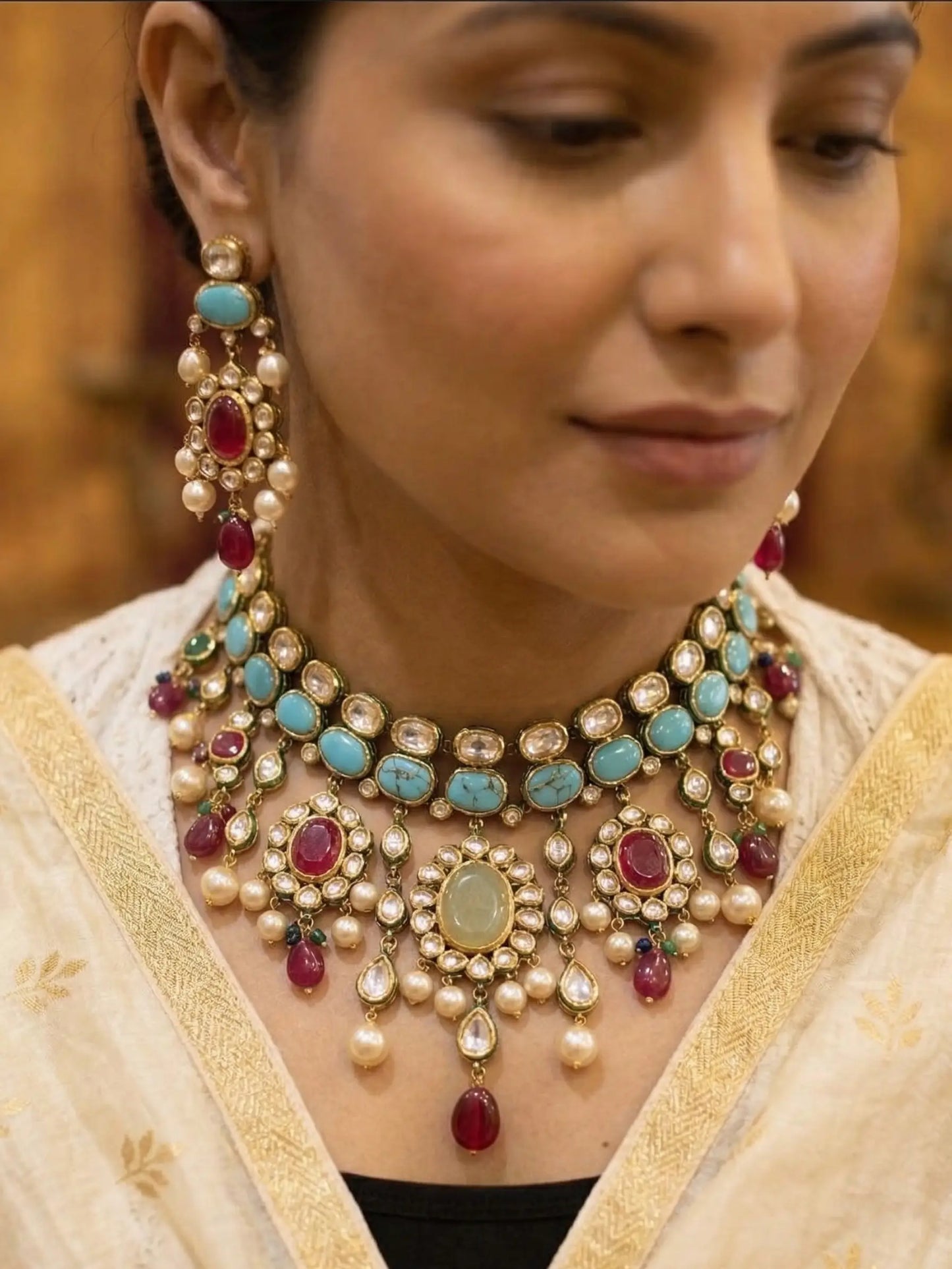 Woman wearing a detailed necklace with pearls, turquoise stones, and red gemstones.