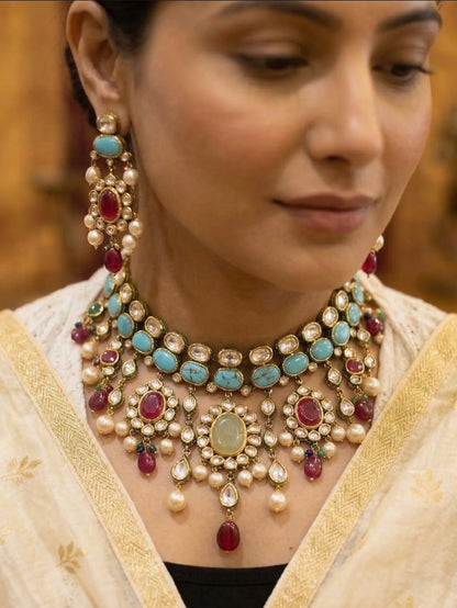 Woman wearing a detailed necklace with pearls, turquoise stones, and red gemstones.