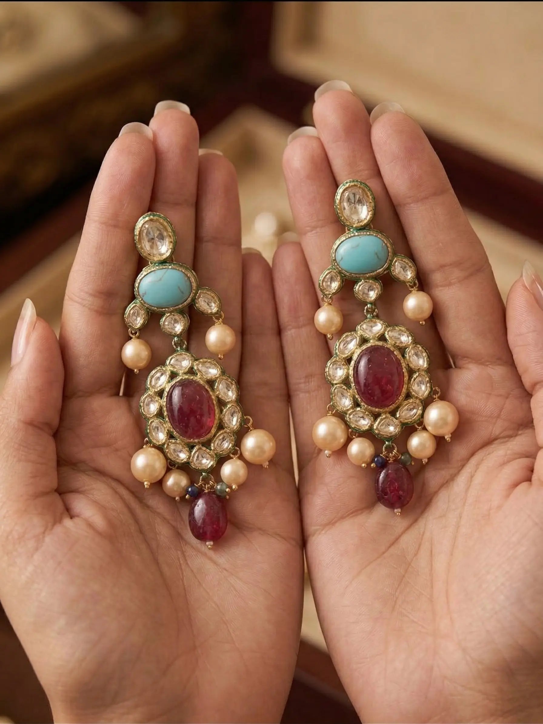 Ornate earrings with gemstones held in hands against a blurred background
