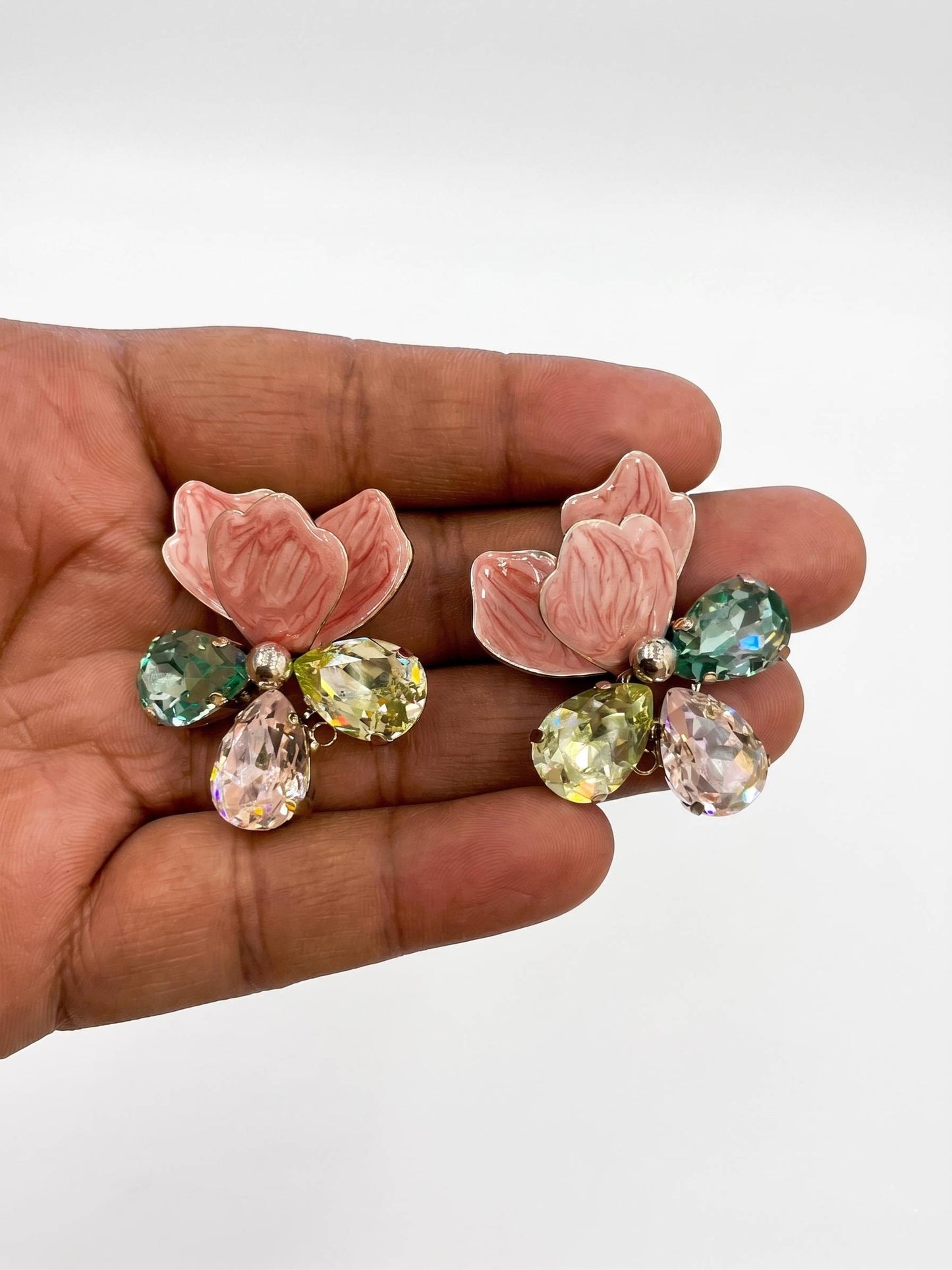 Pink floral earrings with gemstones held in a hand against a white background